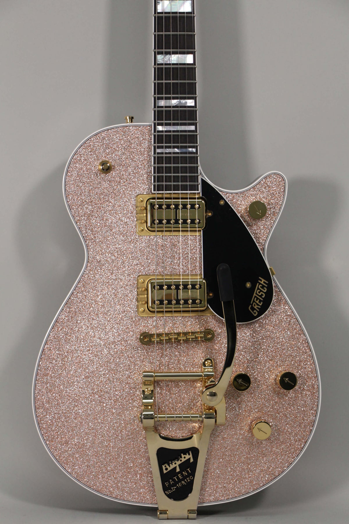 Full-frame, top-down view of a rose gold sparkle guitar with gold hardware, black pickguard, and a Bigsby vibrato.