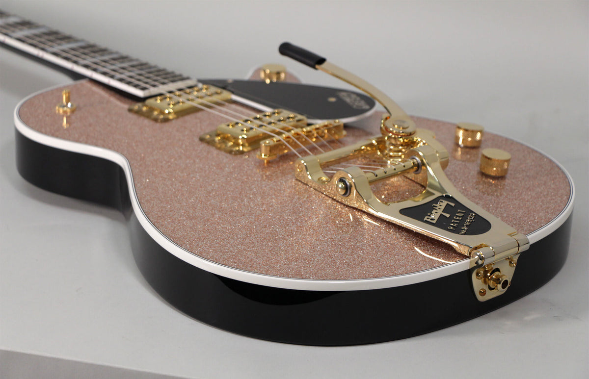 The rose gold sparkle top of this electric guitar is framed from the lower bout, showing gold hardware and a Bigsby tremolo.