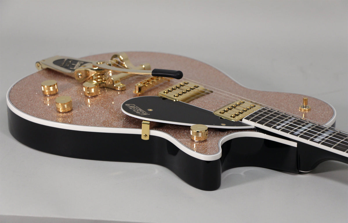 Close-up of a rose gold sparkle guitar body with black sides, white binding, gold hardware, and a black pickguard.
