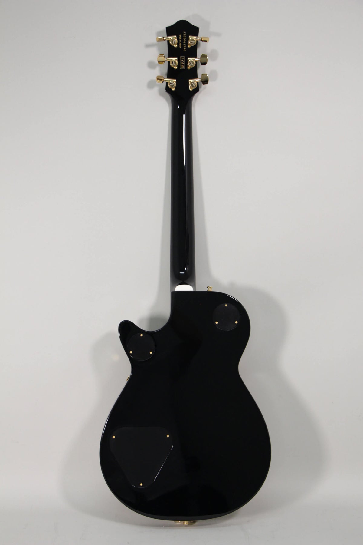The back of a black sparkle guitar with a glossy finish, gold tuners, and three black control cavity covers.