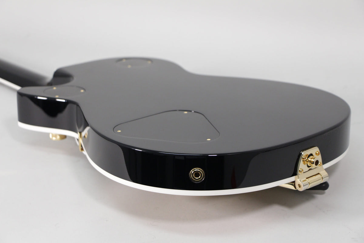 The guitar's glossy black back and side are angled, revealing white binding, a gold output jack, and a gold strap button.