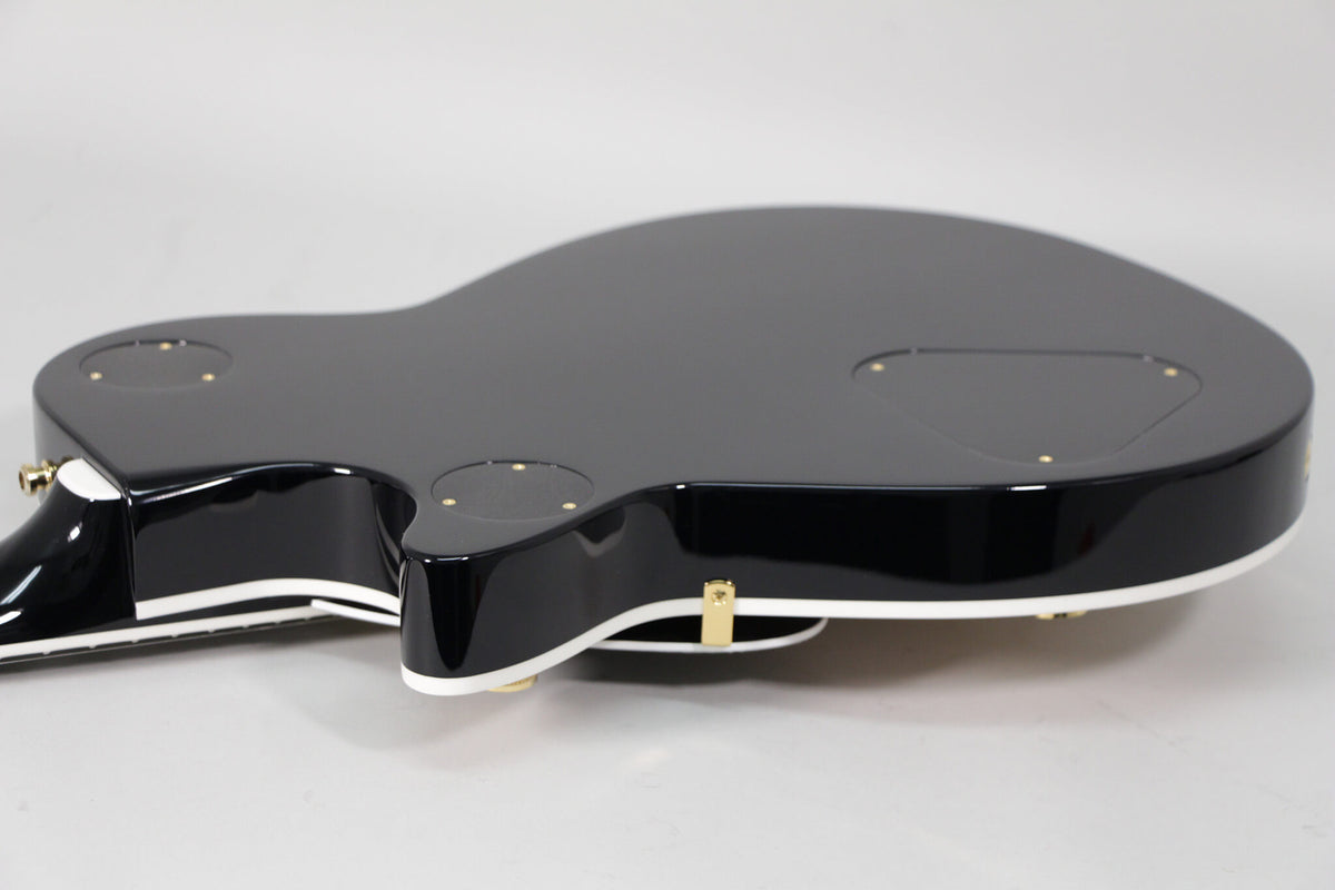 The glossy black guitar body, with white binding, is angled to show the back with three gold-screwed control plates.