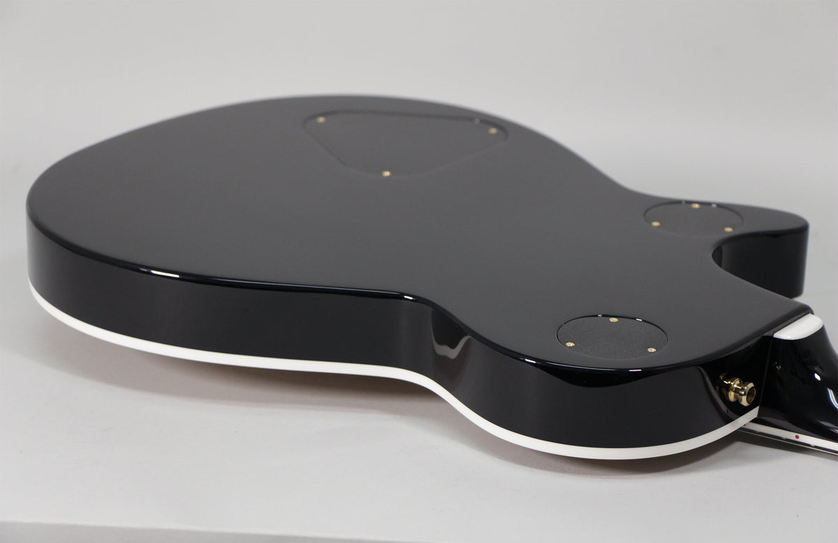 The guitar's glossy black back, with white binding, shows three control cavity covers and a gold output jack.