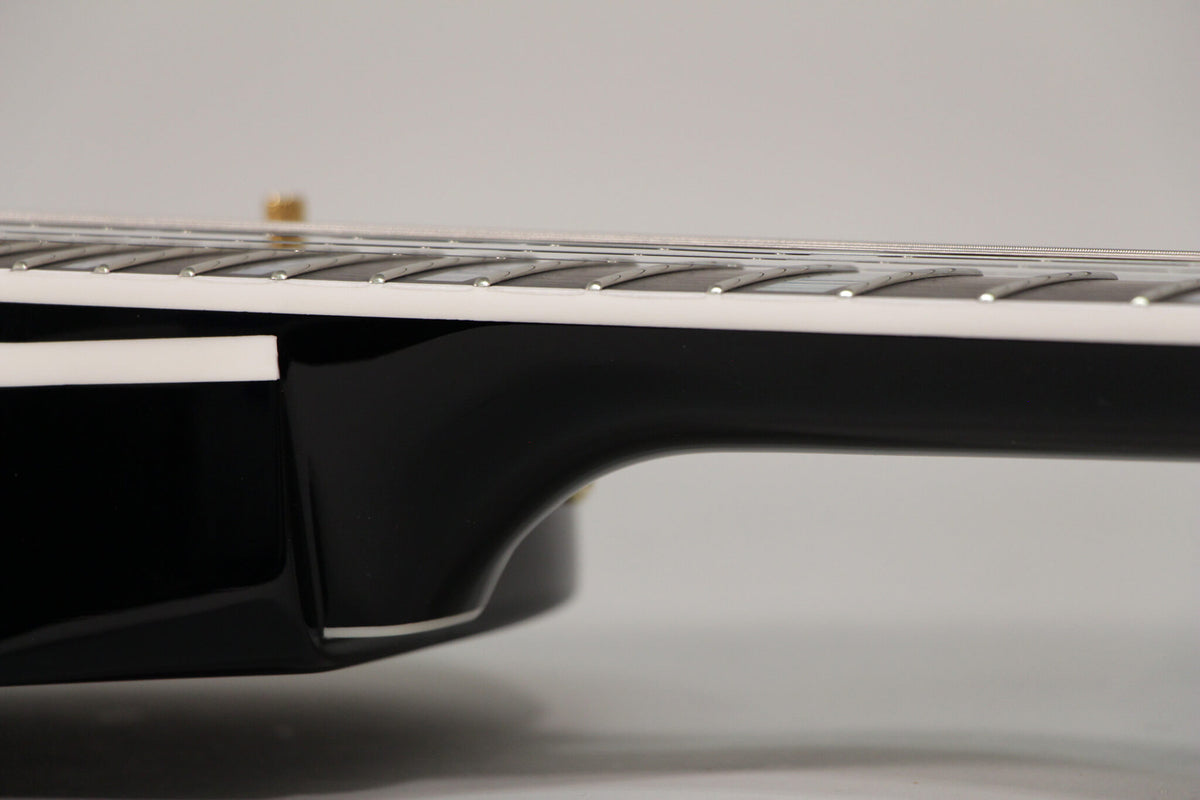 Close-up of the guitar's black body and neck joint, showing the white binding along the fretboard and body edge.