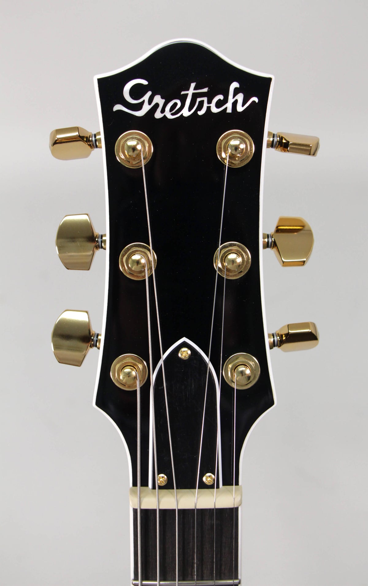 Close-up of the black headstock with white binding, gold tuners, and a white nut, viewed from the front.