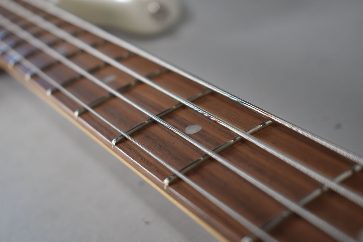 Close-up of the bass's dark wood fretboard with four strings and white dot inlays, angled from the headstock towards the body.