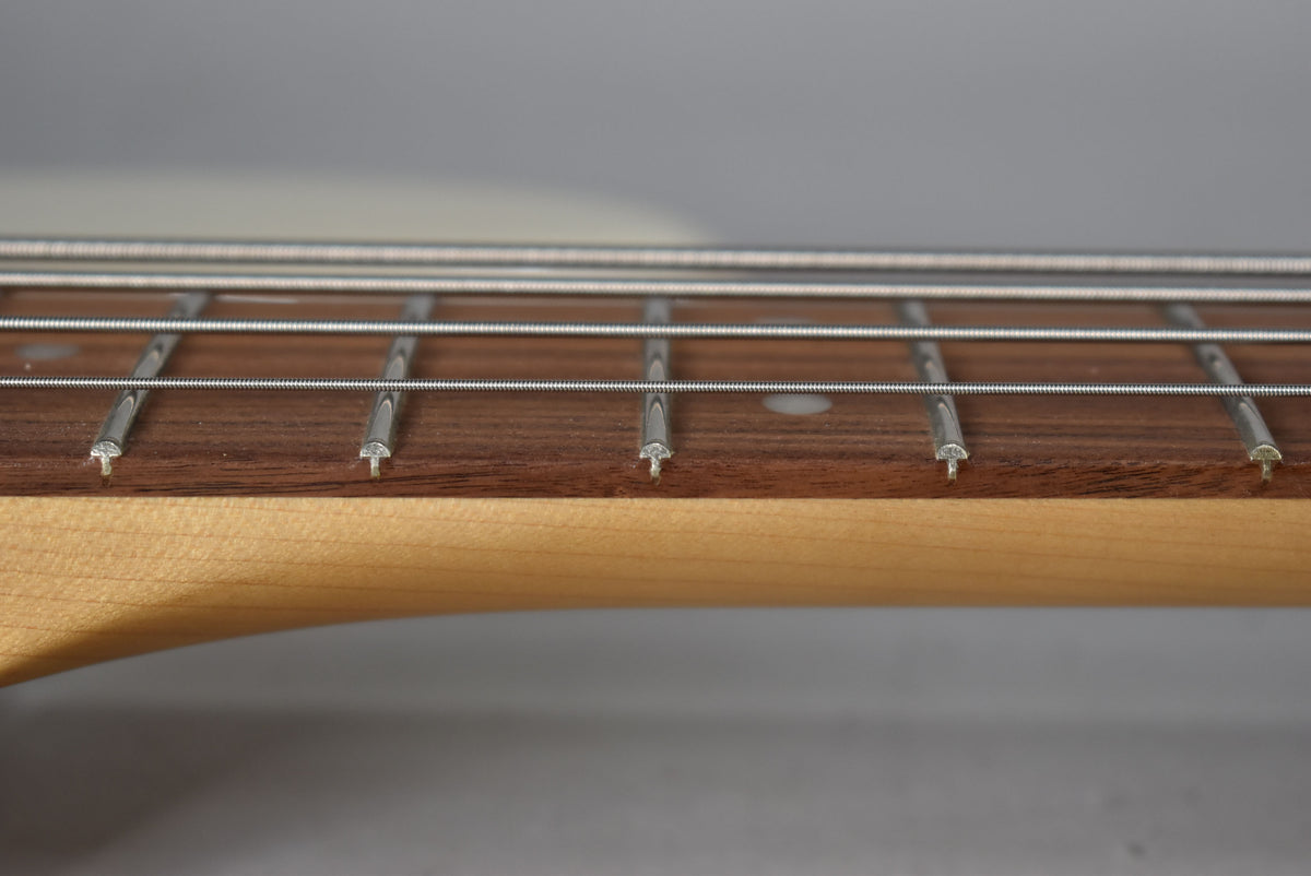 Close-up of the bass's dark wood fretboard with four strings, silver frets, and white dot inlays, against a light maple neck.