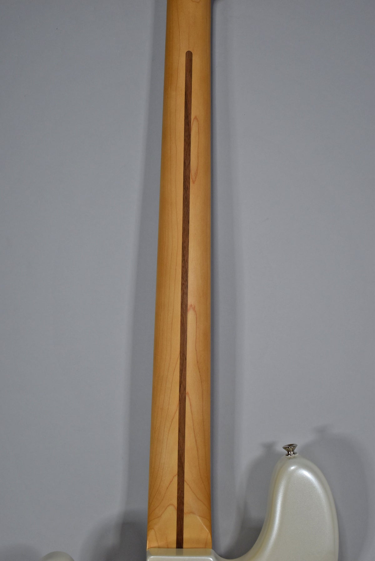 The back of the bass neck, light wood with a dark wood stripe, extends from the pearlescent white body to the top of the frame.