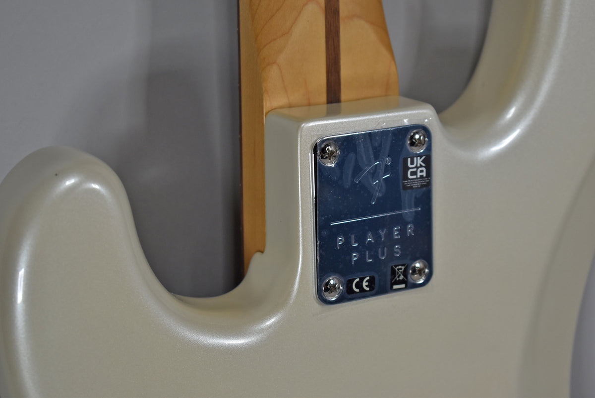 Close-up of the bass's pearlescent Olympic Pearl body and the chrome neck plate, which has "PLAYER PLUS" and regulatory marks.