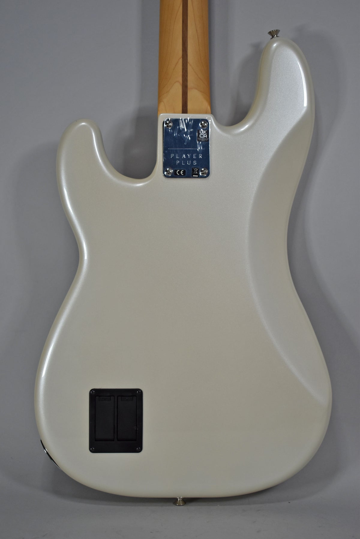 The bass guitar's pearlescent white body, with a visible battery compartment and neck plate, is viewed from the back.