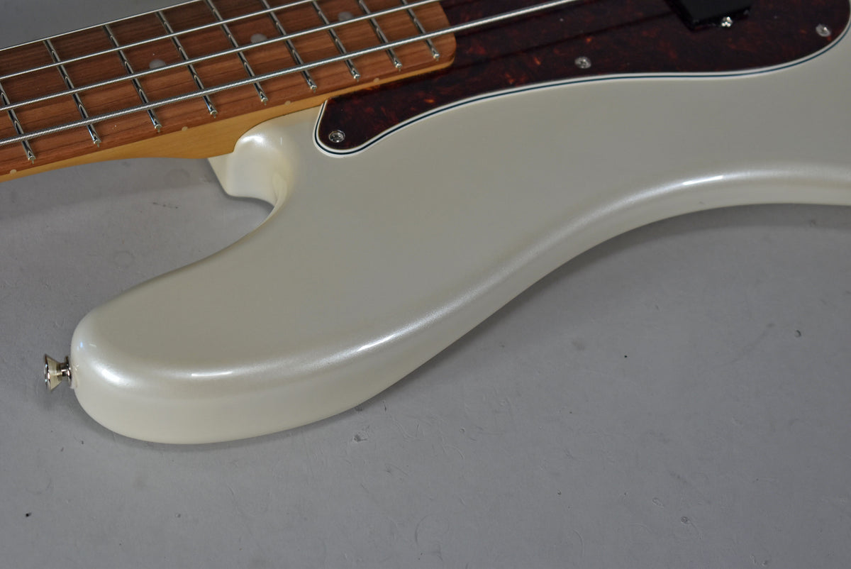Close-up of the bass's lower body, showing the pearlescent Olympic Pearl finish, a tortoiseshell pickguard, and the neck joint.