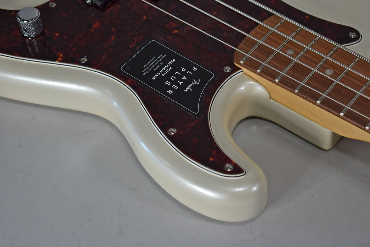 Close-up of the bass body's lower horn in Olympic Pearl, showing the tortoise pickguard, a chrome knurled knob, and part of the fretboard.