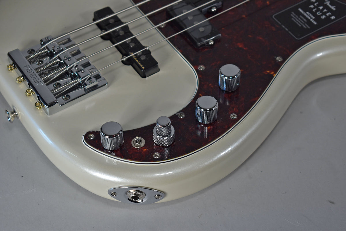Close-up of the bass body, showing the pearlescent white finish, tortoiseshell pickguard, chrome bridge, and four knurled chrome control knobs.
