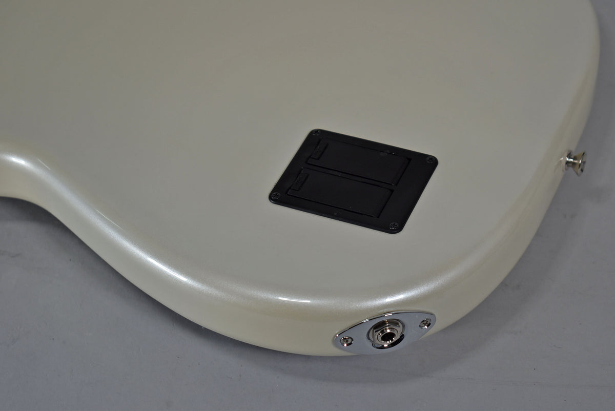 The lower bout of a pearlescent white bass, showing the chrome output jack and a black rectangular battery compartment.
