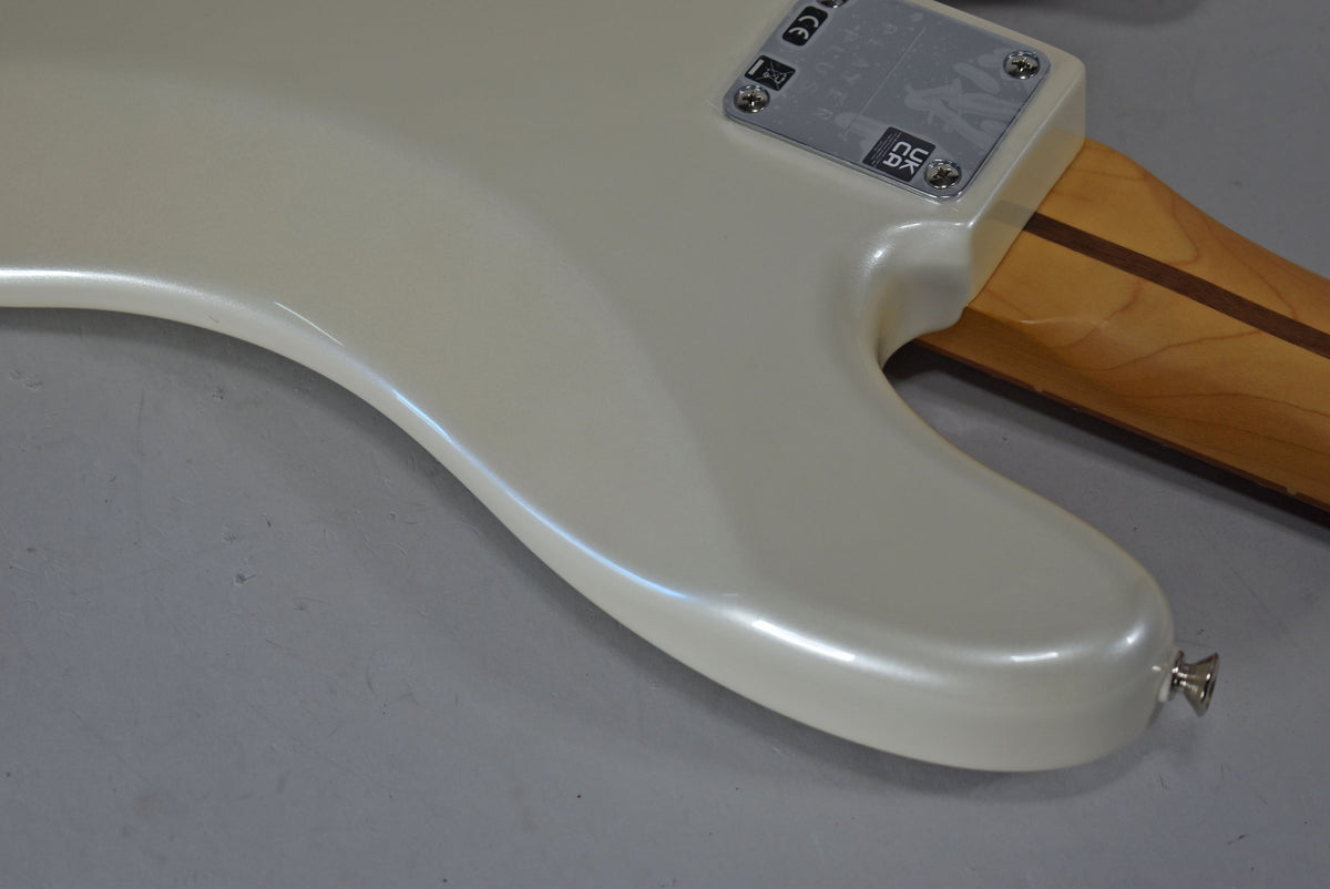 The bass's pearlescent white body curves into a neck plate with visible CE and UKCA marks, and a light wood neck.