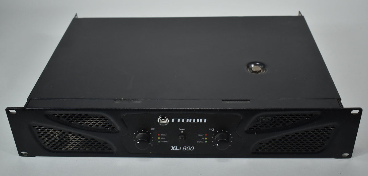 A black power amplifier, viewed from above and slightly to the front, with two large grilles and two control knobs on the front panel.