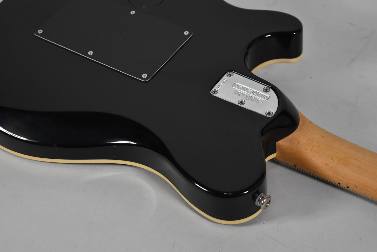 The guitar's glossy black back, with cream binding, shows a control cavity cover, a chrome neck plate, and the input jack.