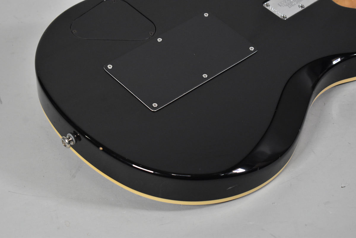 The guitar's black back with cream binding is angled, showing two control plates, a strap button, and light surface wear.