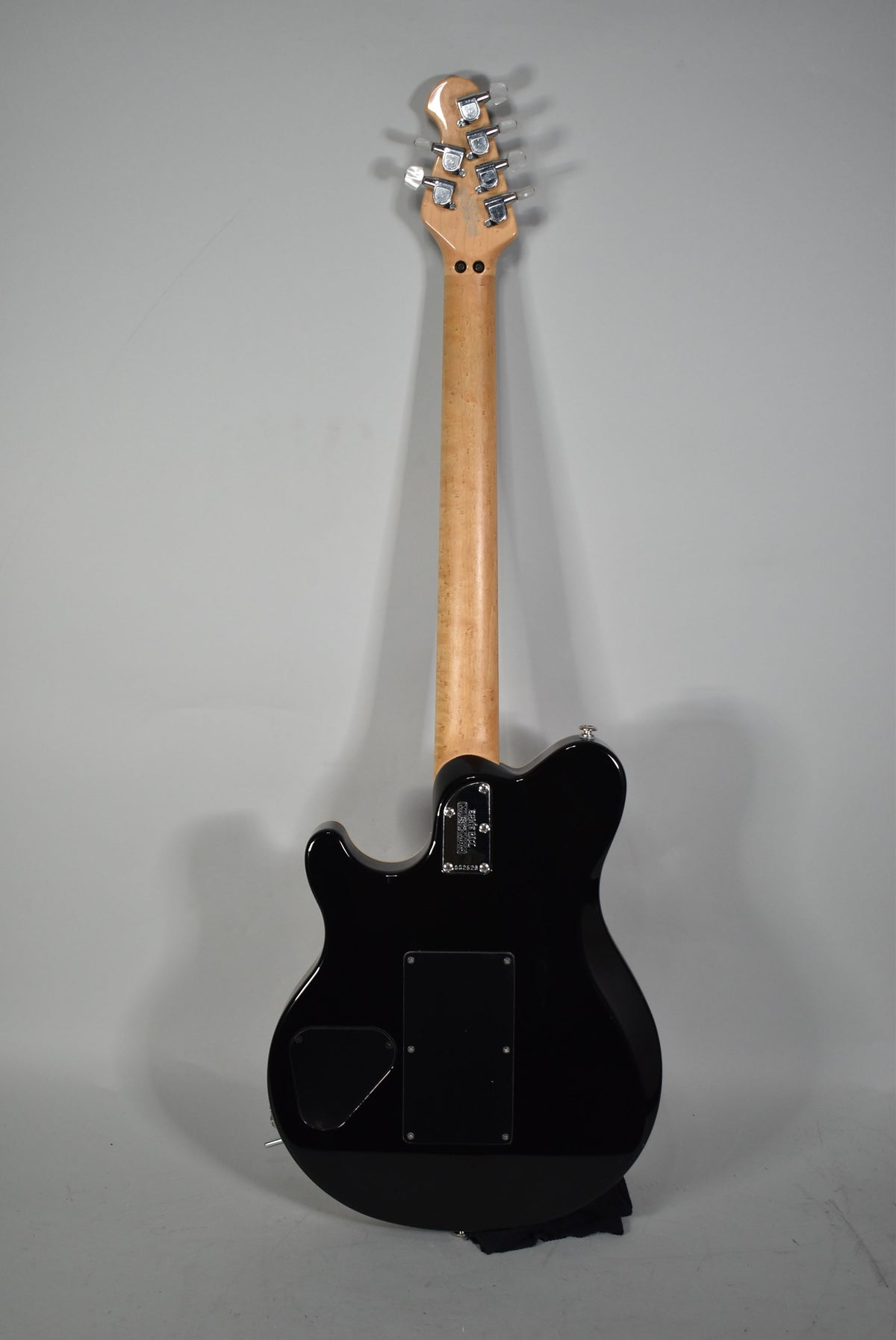 Full rear view of a black electric guitar with a light maple neck and headstock, showing chrome tuners and control cavity covers.