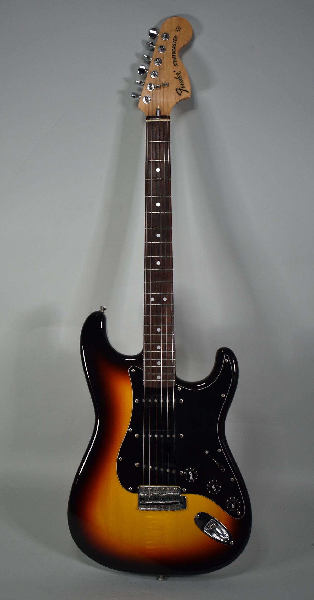 Full-length view of a glossy three-tone sunburst Stratocaster with a black pickguard, three single-coil pickups, and chrome hardware.