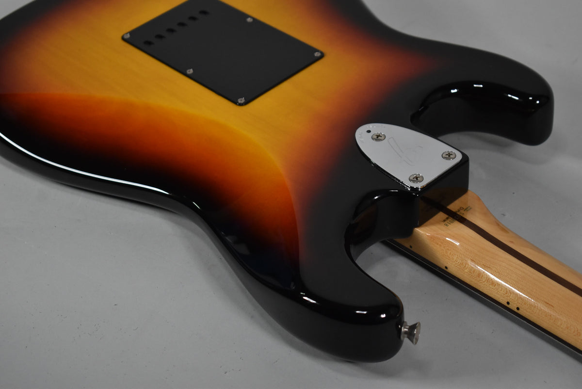 The guitar's glossy three-tone sunburst body is seen from the back, showing the black tremolo cover, chrome neck plate, and strap button.