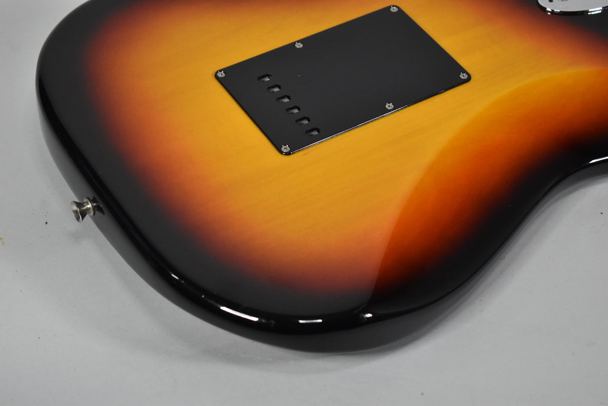 The guitar's glossy three-tone sunburst back shows a black tremolo cavity cover with six string holes and a chrome strap button.