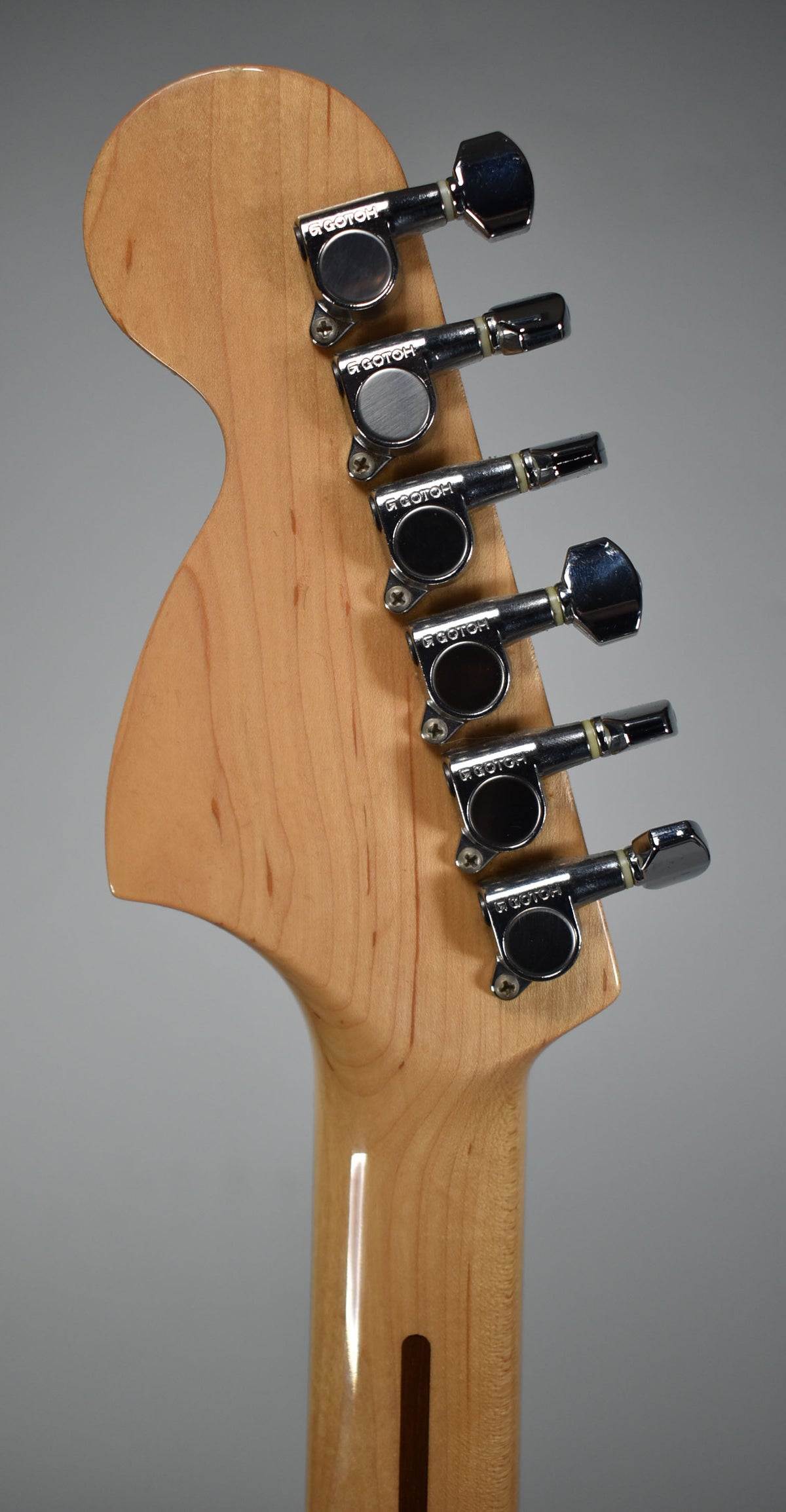 The back of the light-colored headstock and upper neck, showing six chrome tuners and a small chip on the top edge.