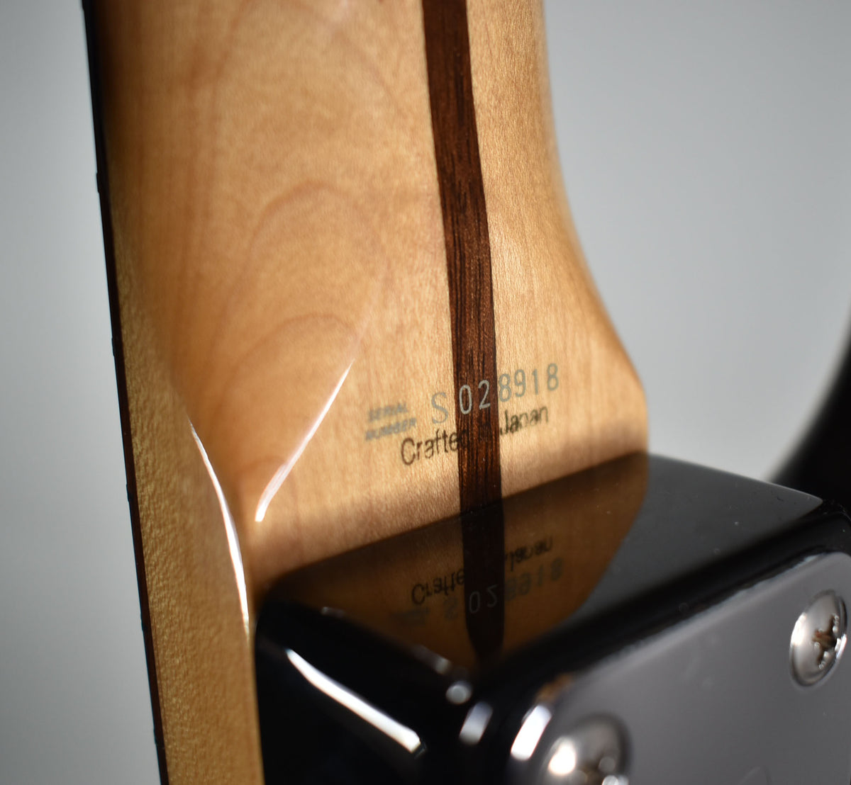 Close-up of the guitar's light wood neck heel with a dark stripe, showing the serial number and "Crafted in Japan" stamp.