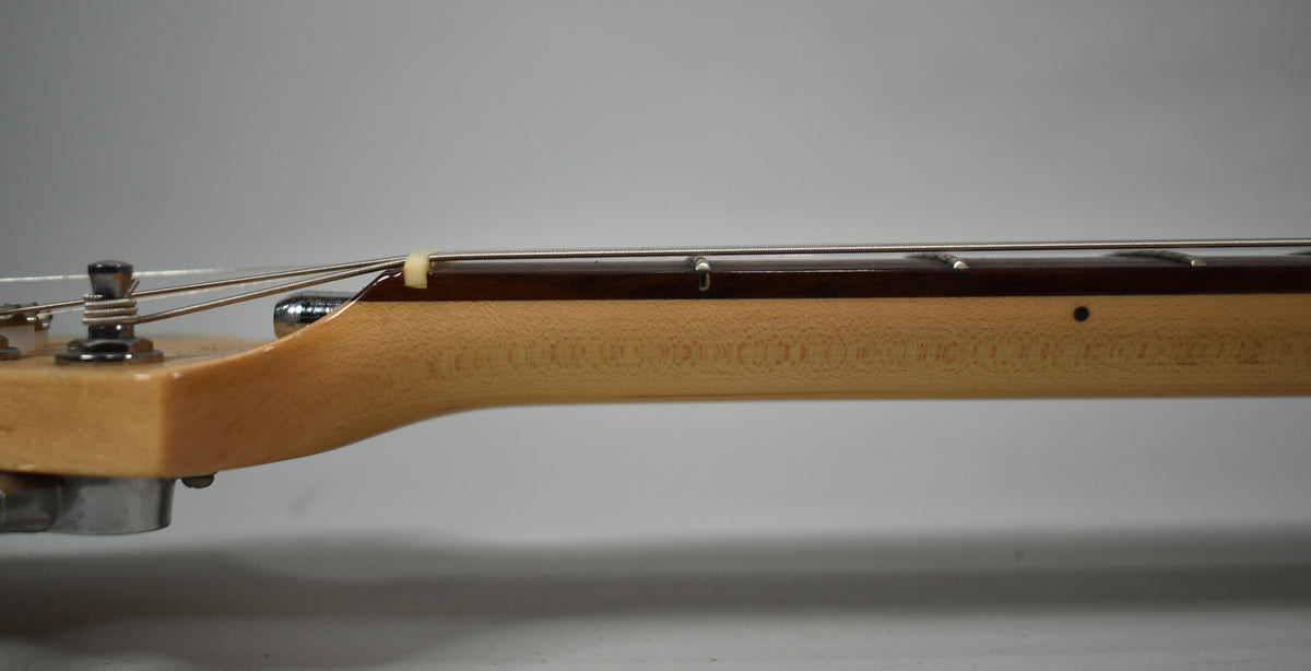 The guitar's light maple neck and dark fretboard are seen from the side, with a string tree and tuning peg visible.