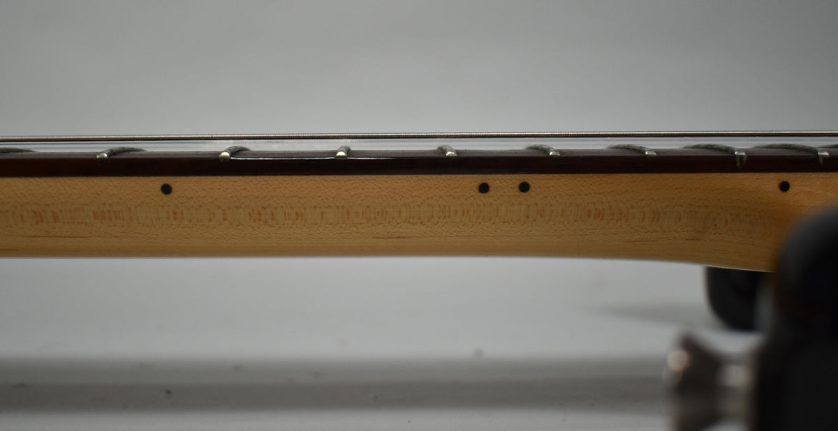 The guitar's light maple neck and dark fretboard are seen from the side, revealing black dot markers and shiny frets.