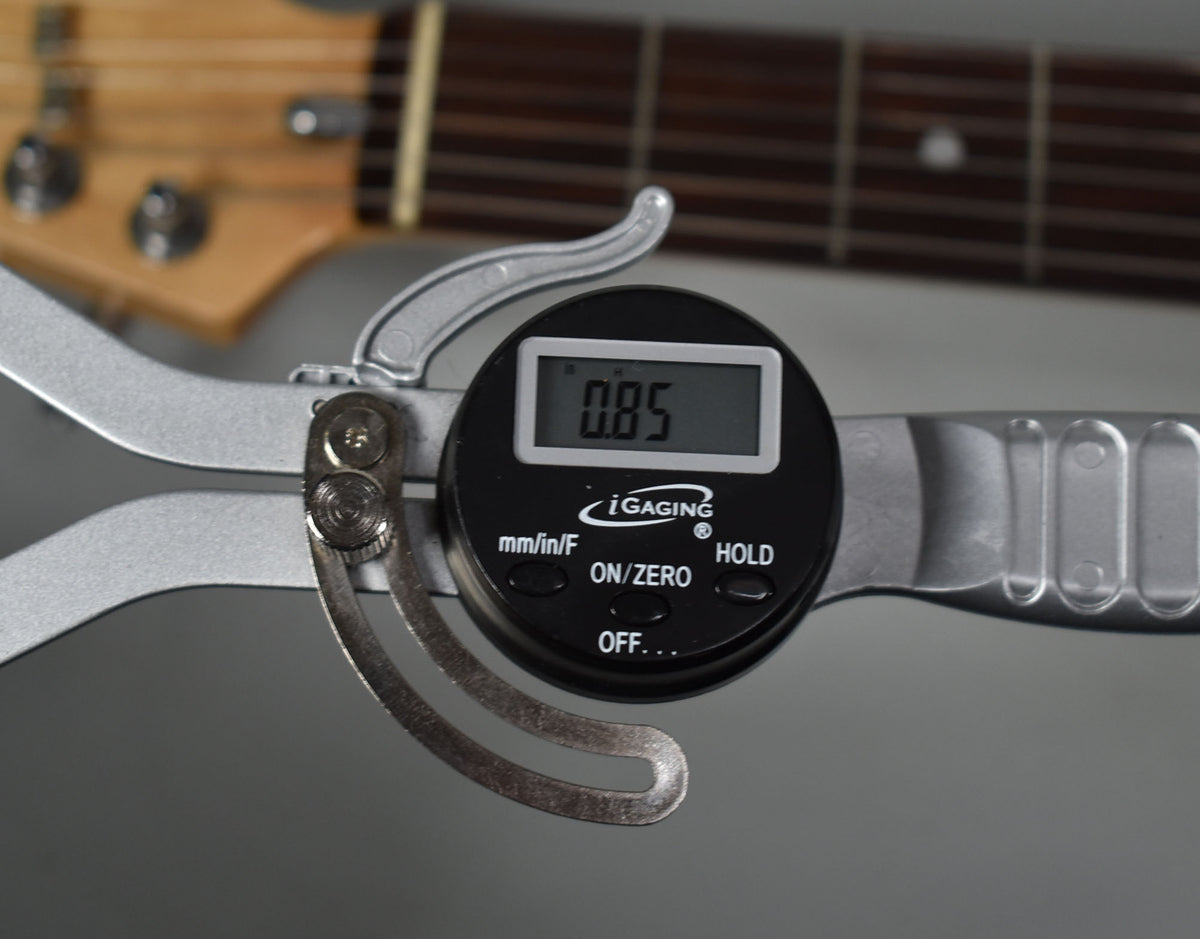 A digital caliper measures fret height at 0.85mm on the dark rosewood fretboard of a maple neck.