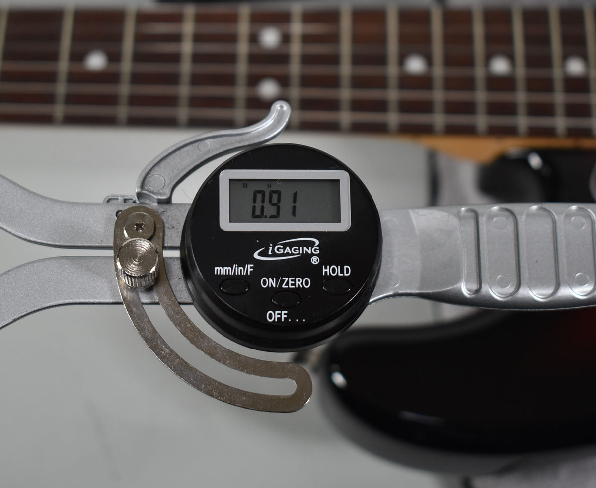 A digital caliper measures fret height at 0.91mm on the rosewood fretboard with dot inlays, over the sunburst body.