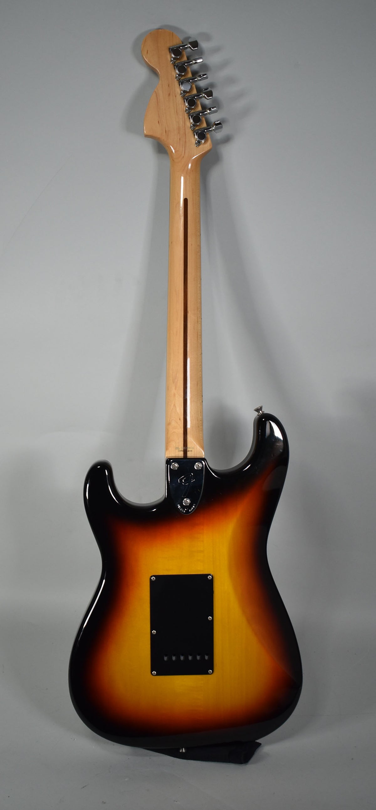 The guitar's back, neck, and headstock are visible, showing a three-tone sunburst finish with a black tremolo cover and chrome tuners.