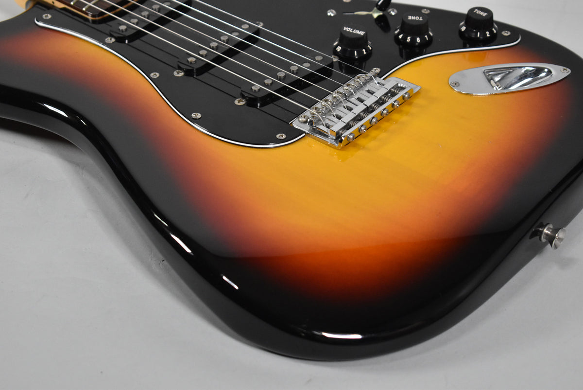The guitar's glossy three-tone sunburst body, black pickguard, and chrome hardware are visible from the lower bout to the bridge.