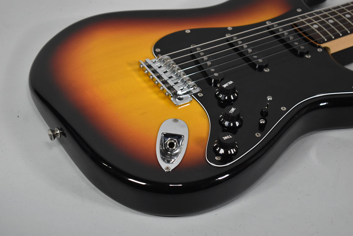 Close-up of the guitar's lower body, showing the three-tone sunburst finish, black pickguard, chrome bridge, and three black control knobs.