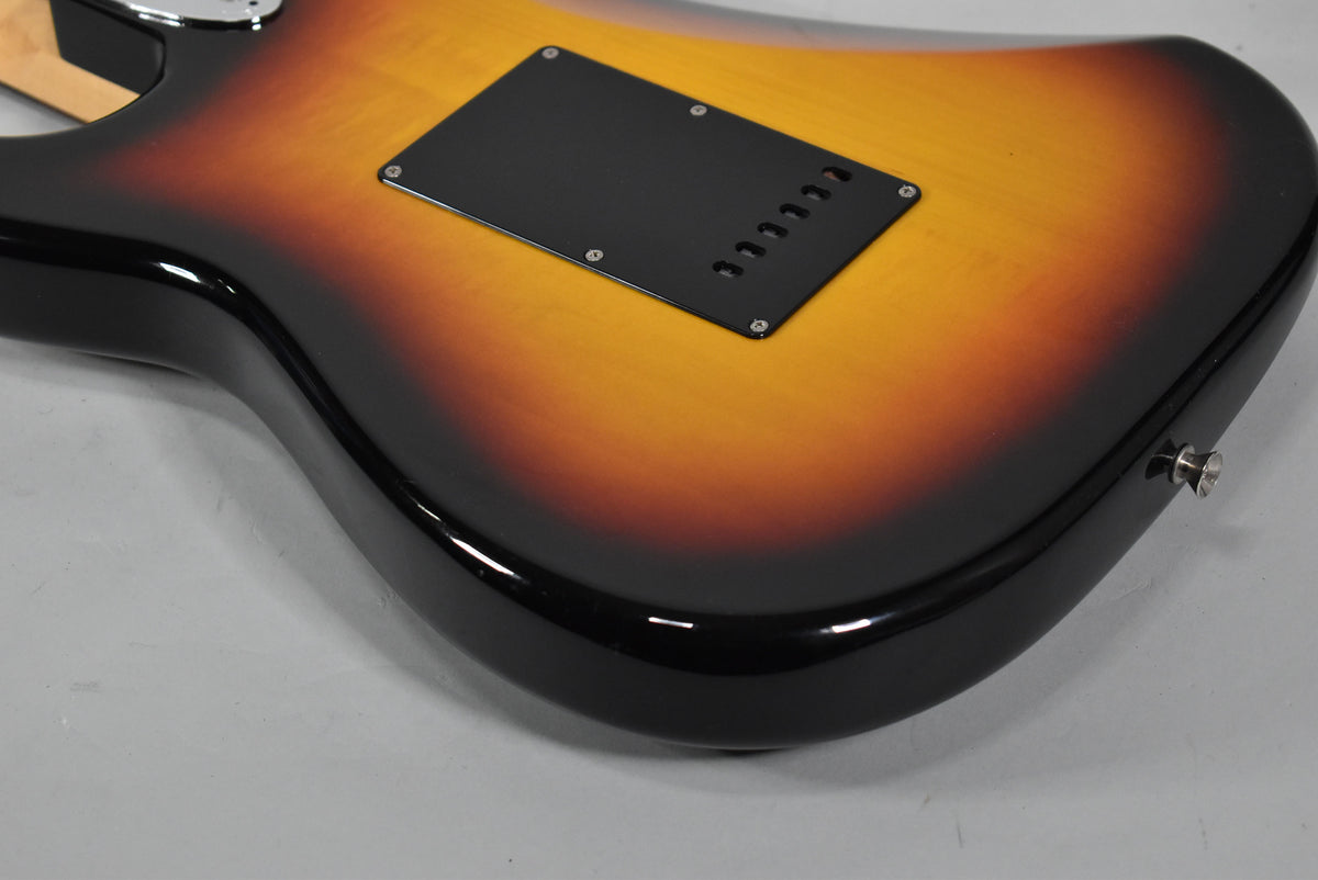 The guitar's glossy three-tone sunburst back, with a black tremolo cavity cover and chrome output jack, is angled from the lower bout.