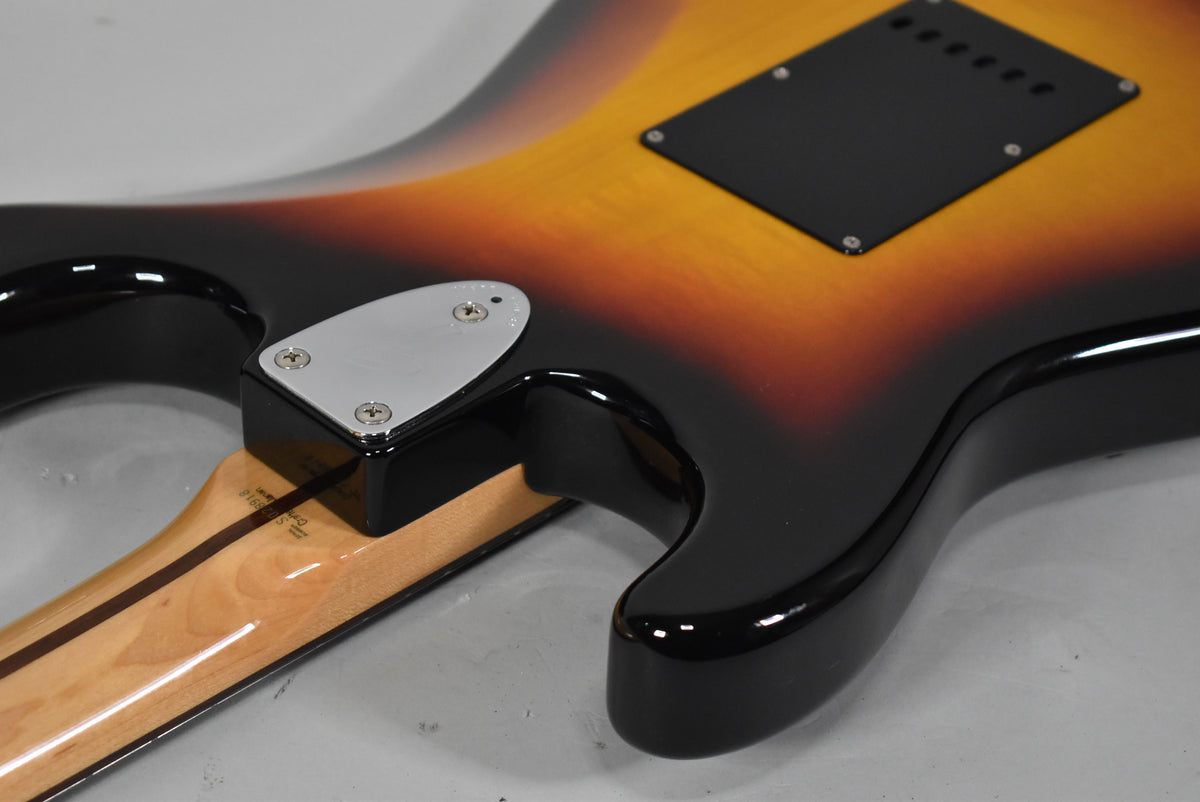 The guitar's glossy three-tone sunburst body, with a black tremolo cover and chrome neck plate, meets a light wood neck.