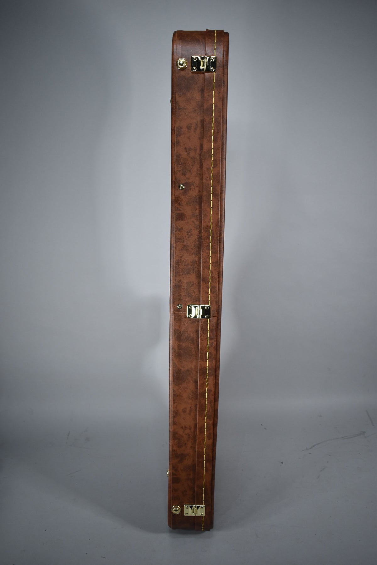 A full-length view of the brown leatherette case, showing its textured finish, gold hardware, and yellow stitching.