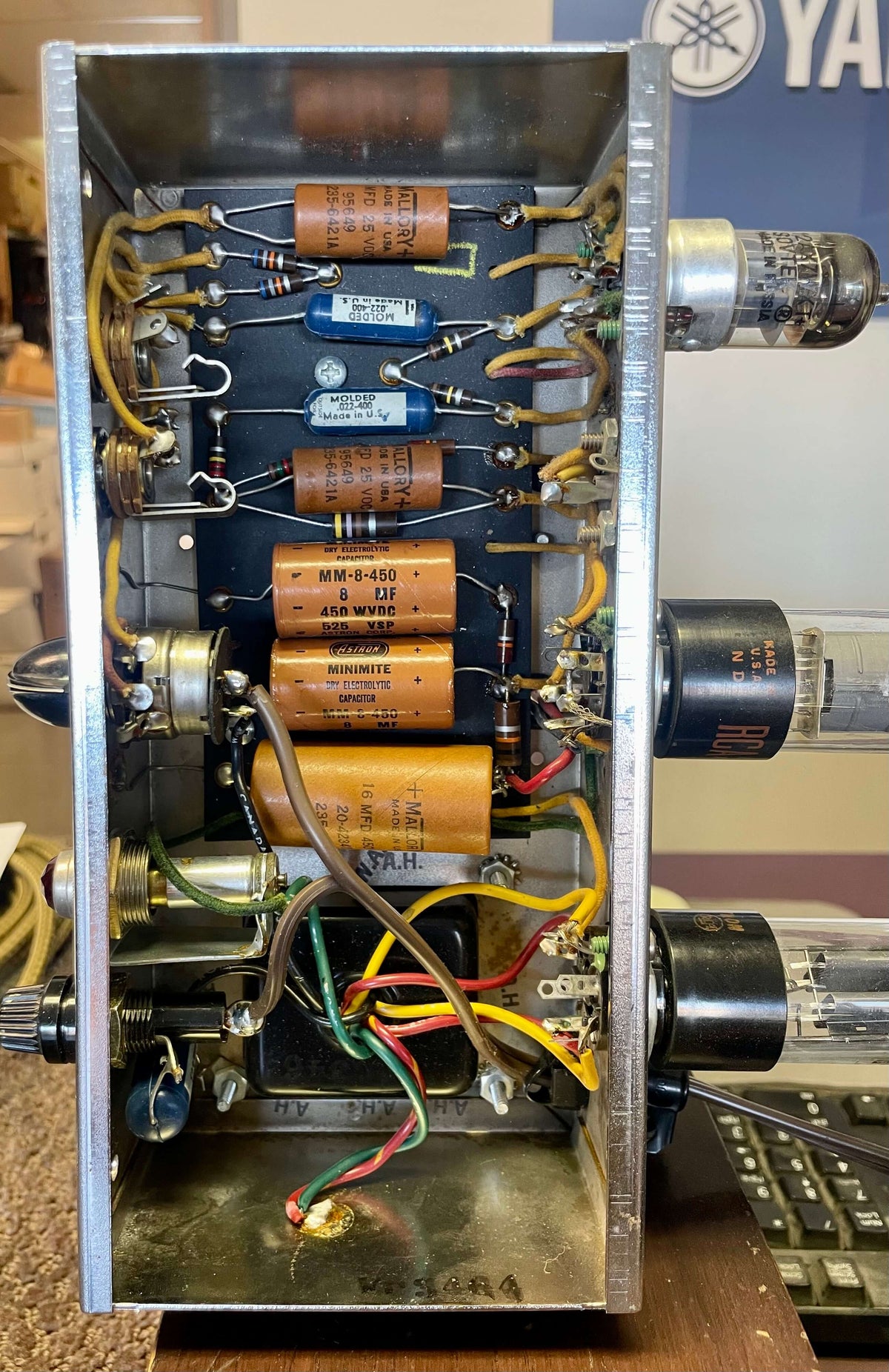 Top-down view of the amp's open chassis, revealing neatly wired orange and blue capacitors, resistors, and three vacuum tubes.