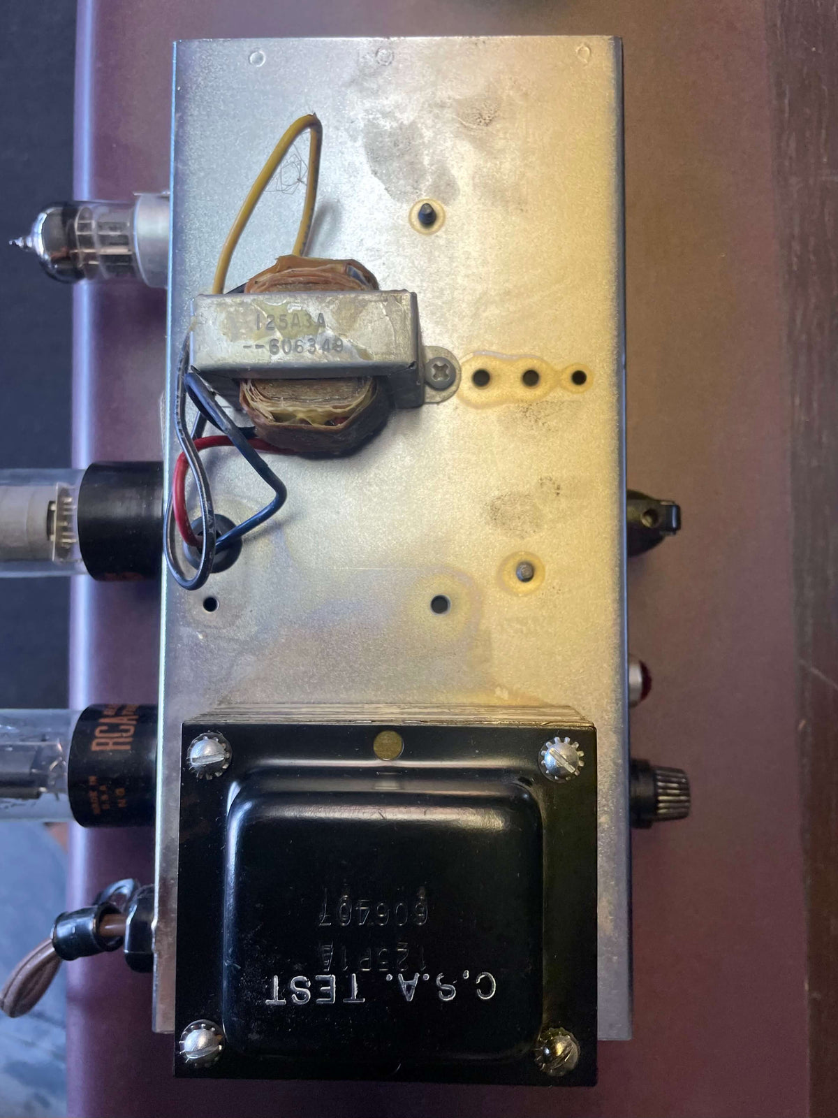 Overhead view of the amp's silver chassis, showing two transformers, exposed wiring, and three vacuum tubes with visible RCA branding.