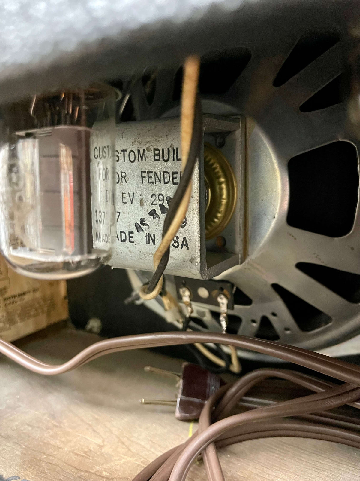 Close-up of the amp's internal components, showing a vacuum tube, speaker magnet, and brown power cable with a two-prong plug.