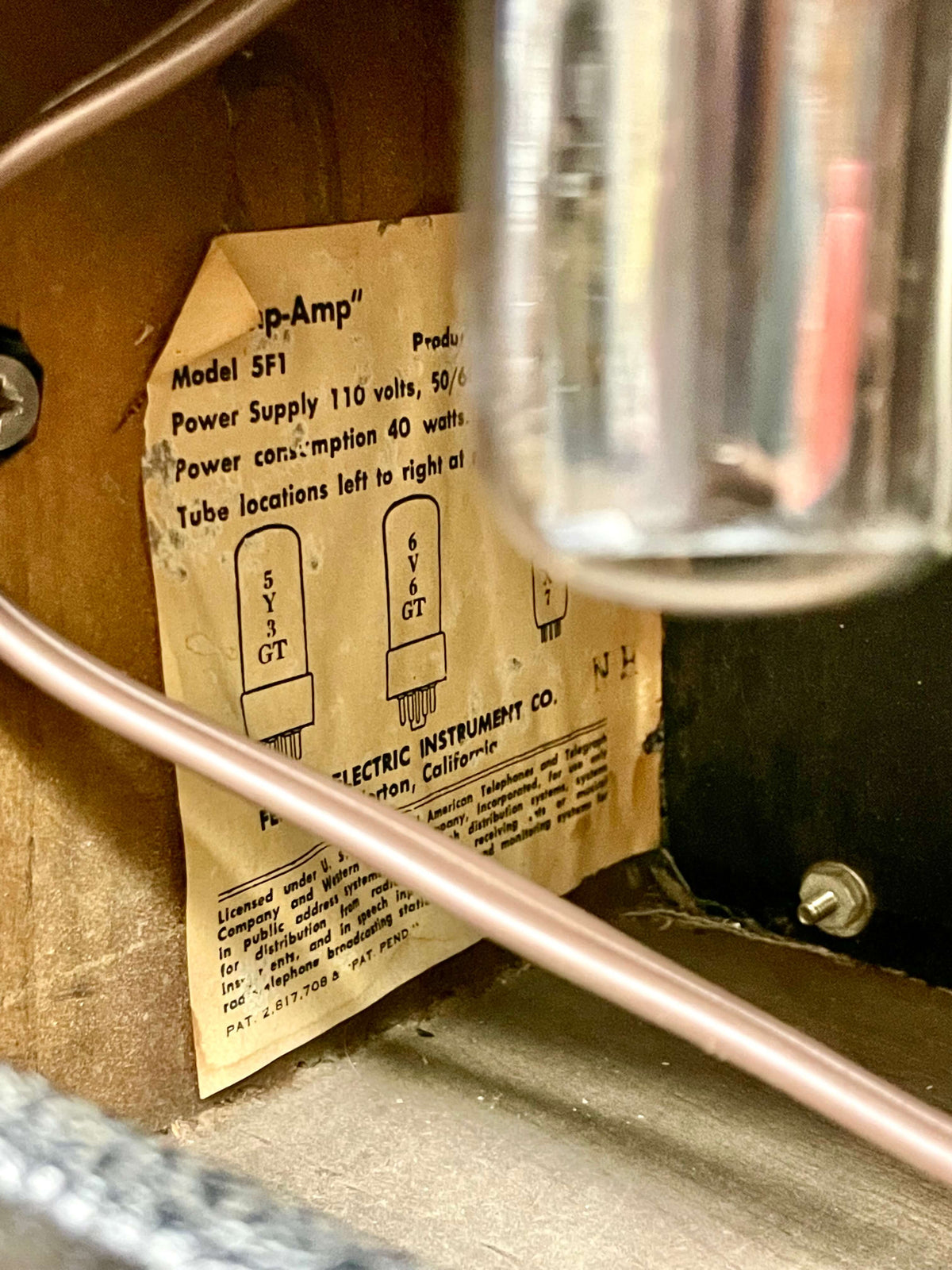 Close-up of the amp's interior, showing a faded, creased tube chart with diagrams and text, partially obscured by a shiny tube and copper wire.