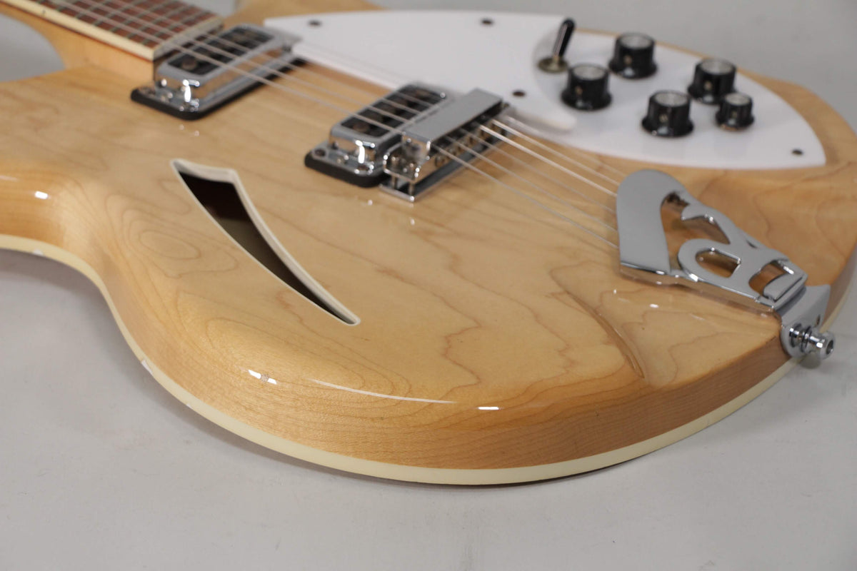 The upper bout of a glossy natural finish guitar, showing the f-hole, chrome bridge, tailpiece, and white pickguard with black knobs.