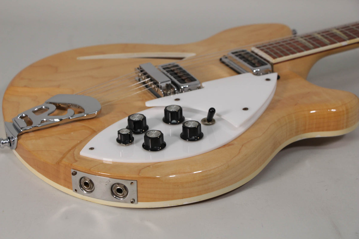 Close-up of the guitar's lower body, showing the light maple finish, white pickguard with five black knobs, and dual output jacks.