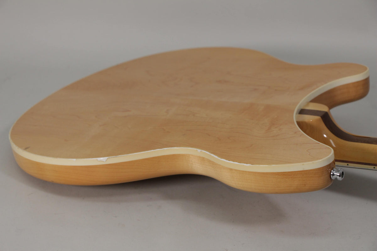 The back of the light blonde guitar body, showing the wood grain, white binding, and a small chip near the lower bout.