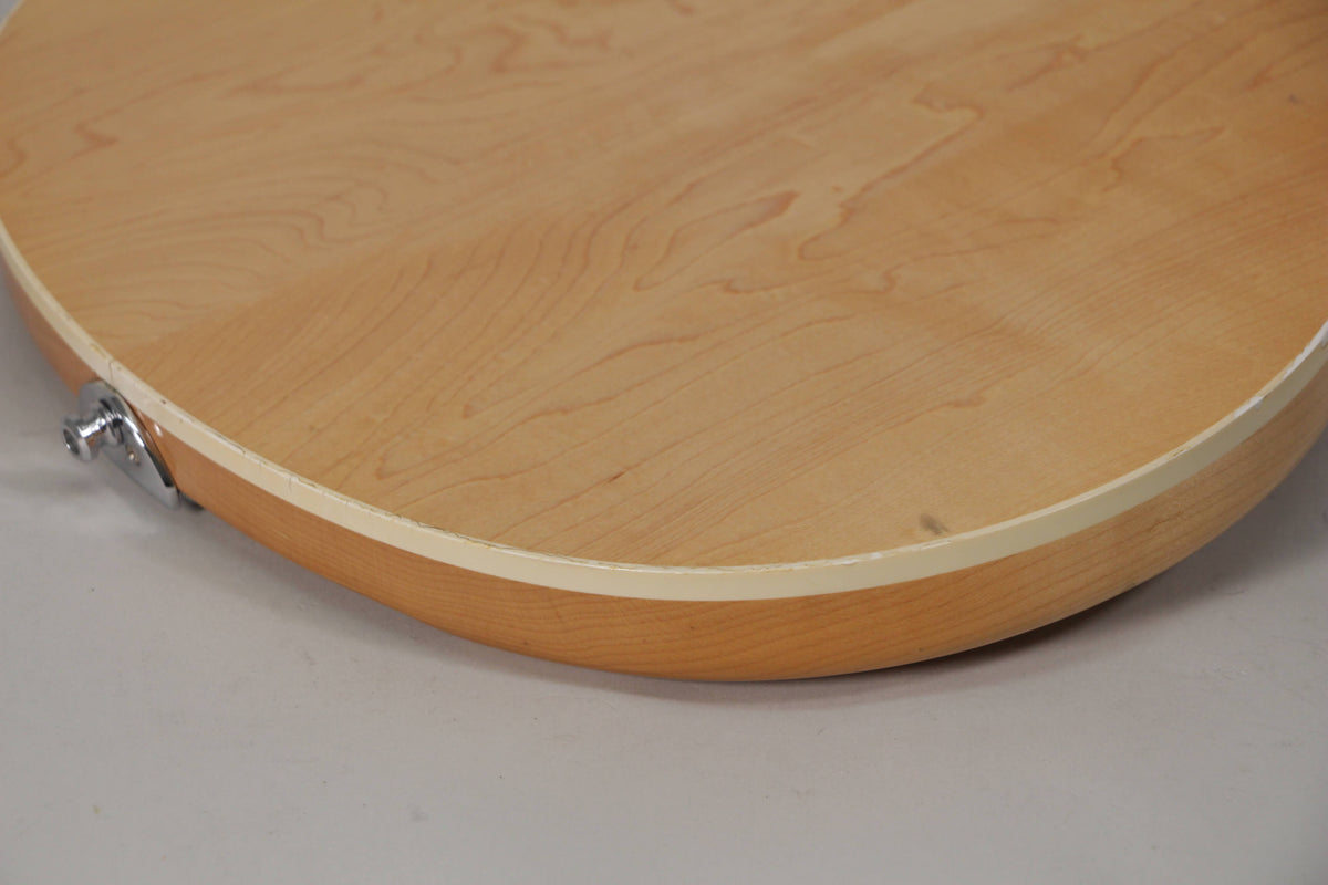 Close-up of the guitar's lower bout, showing the light maple body, cream binding, and a chrome strap button with light wear.