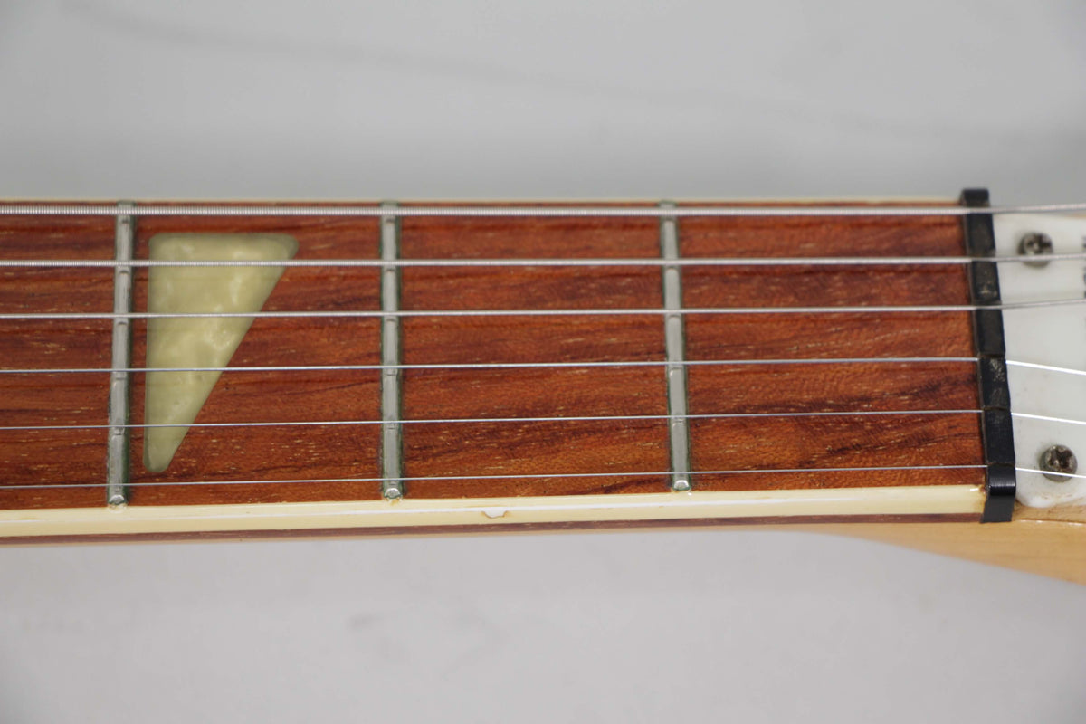 Close-up of the guitar's rosewood fretboard, showing the first five frets, a triangular pearloid inlay, and a small chip on the binding.