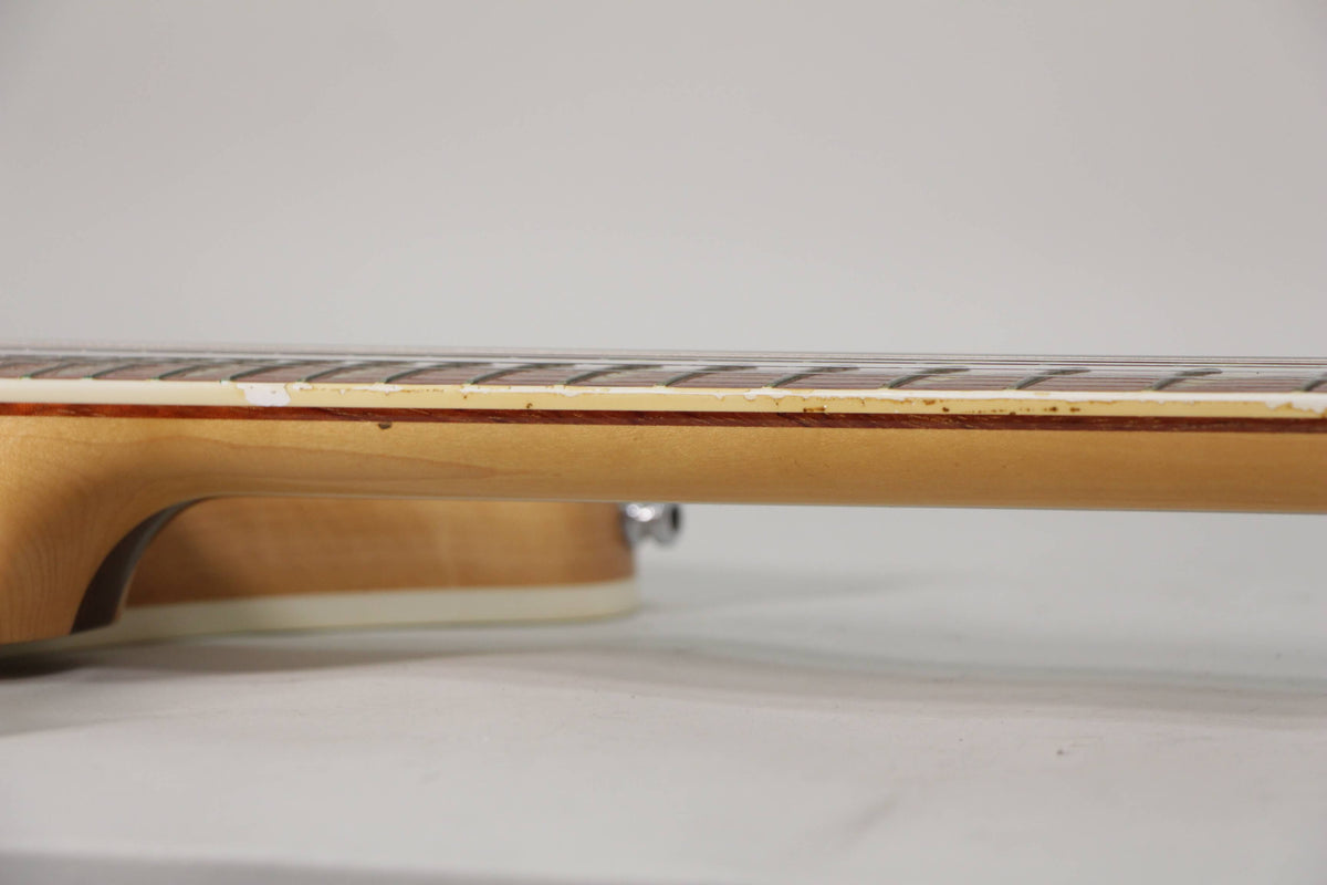 Close-up of the guitar's neck, showing the light maple finish, dark fretboard, and binding with some visible wear and discoloration.