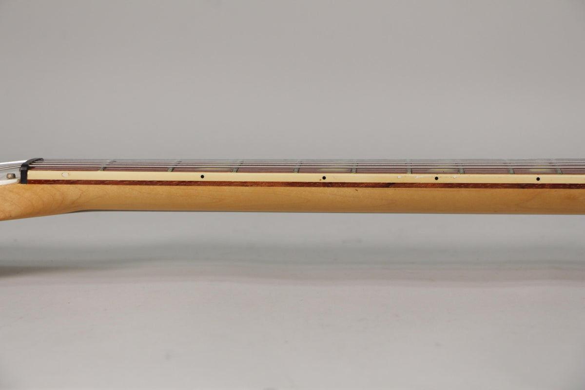 The guitar's light maple neck and dark fretboard are shown from the side, with small black dot inlays and minor wear visible.