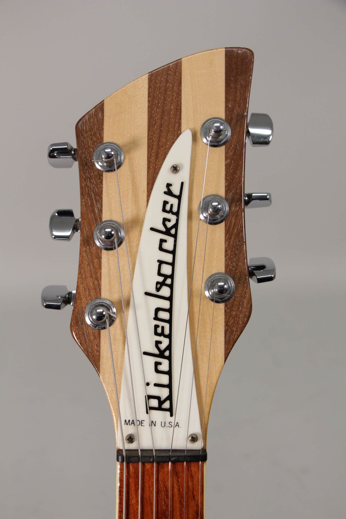 Close-up of the guitar's headstock, showing a striped light and dark wood finish, six chrome tuners, and a white triangular truss rod cover.